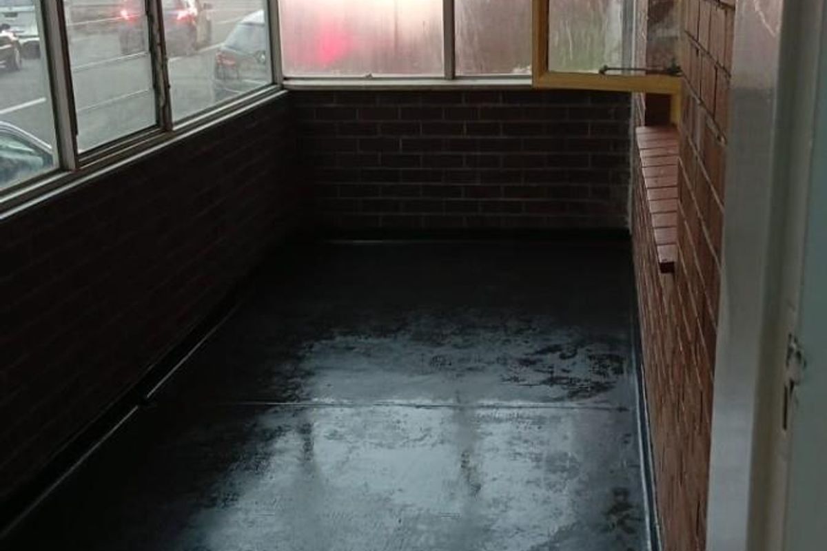 An enclosed balcony or sunroom featuring exposed brick walls, large glass windows, and a dark painted concrete floor.