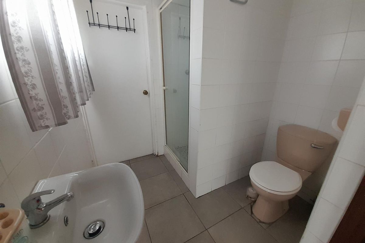 A functional bathroom featuring a shower enclosure, pedestal basin, and toilet with tiled walls and flooring.