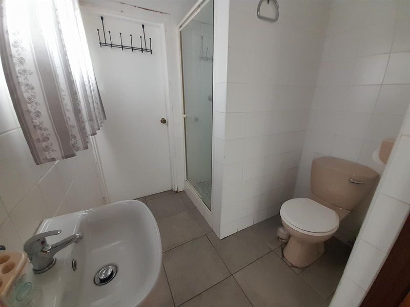 A functional bathroom featuring a shower enclosure, pedestal basin, and toilet with tiled finishes, offering potential for modernization and cosmetic updates.