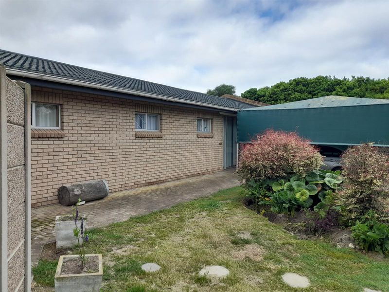 Rear exterior view of the property featuring a brick facade, tiled roof, paved walkway, and a covered carport area.
