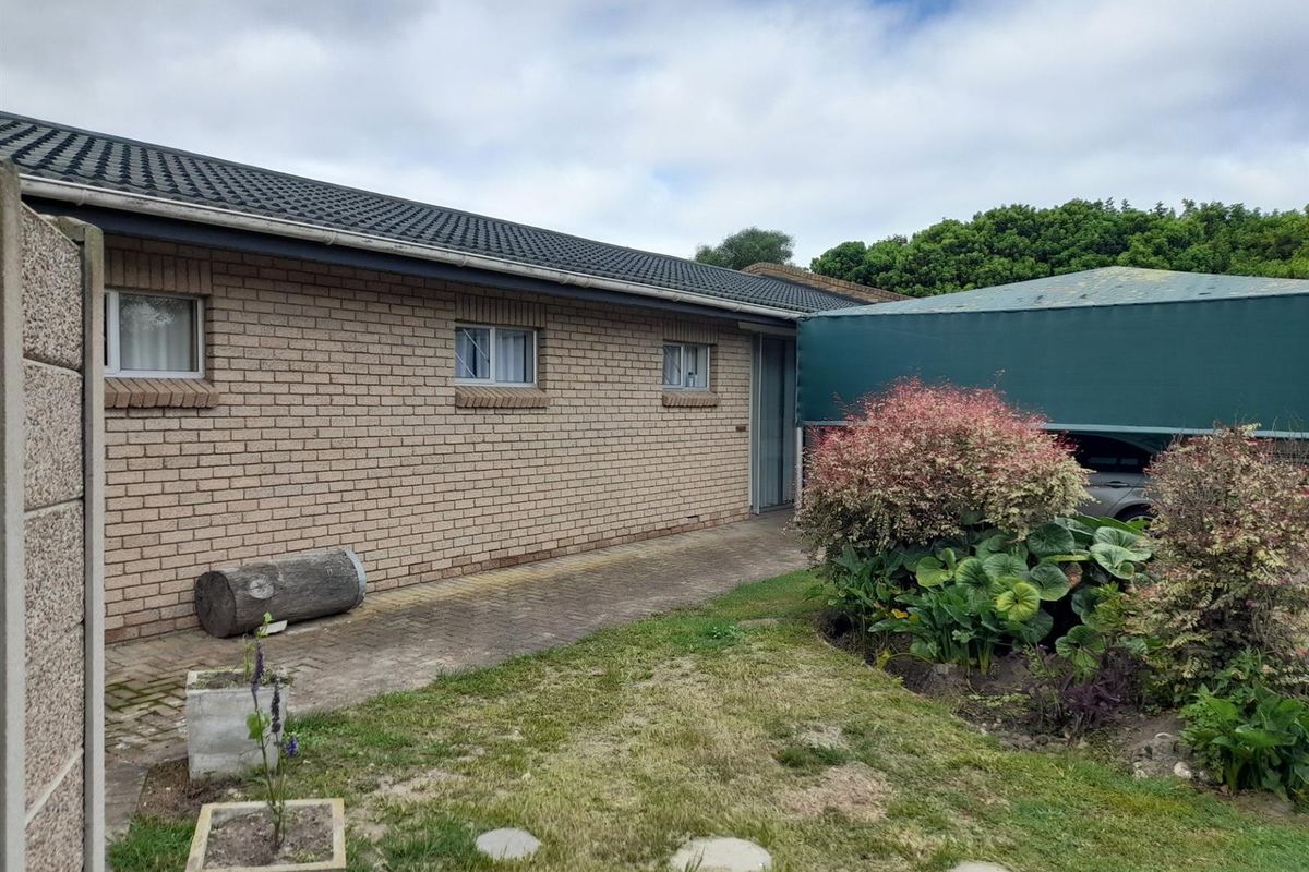 Rear exterior view of the property featuring a brick facade, tiled roof, paved walkway, and a covered carport area.