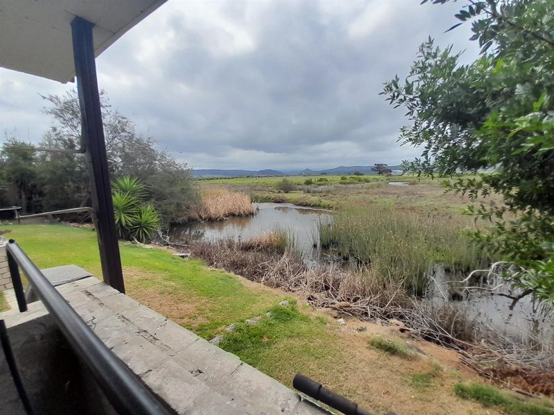 A view from a covered patio overlooking a natural wetland area with reeds and distant hills under a cloudy sky.