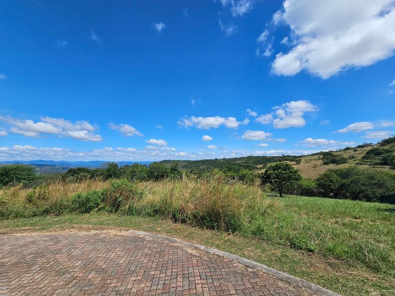 A scenic view of the surrounding landscape and rolling hills from the vacant residential property, featuring a paved driveway edge.