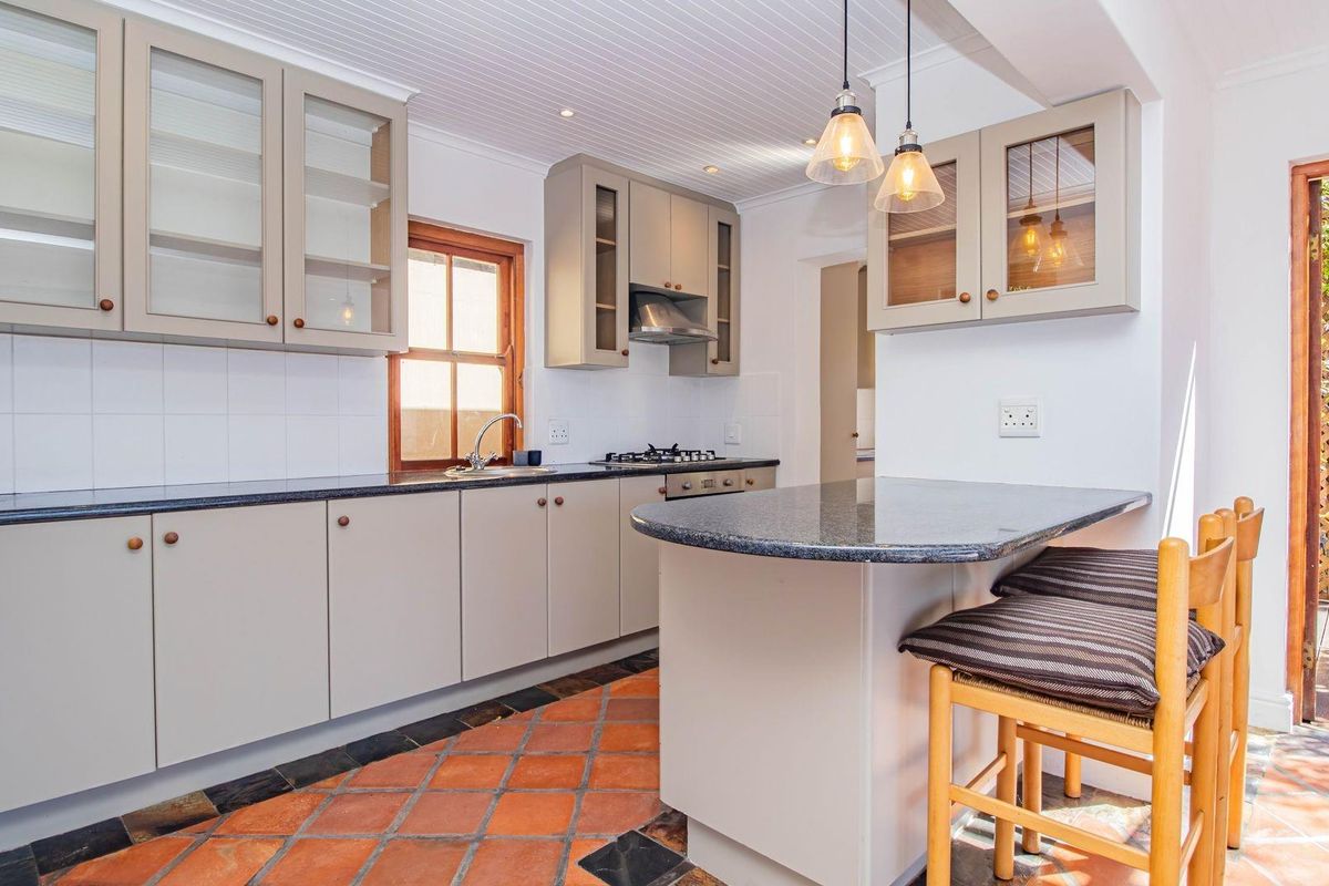 A well-lit kitchen featuring granite countertops, built-in cabinetry, a gas hob, and a breakfast bar, with direct access to an outdoor patio area.