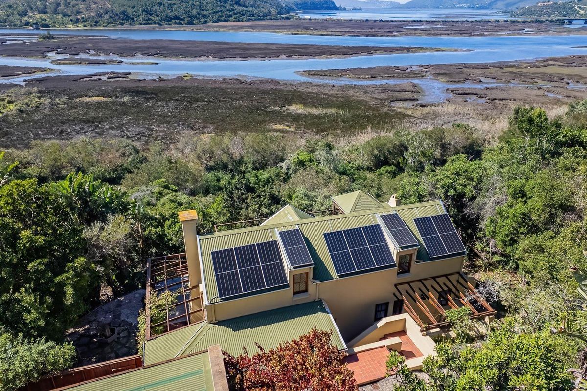 Aerial view of a residential property featuring a metal roof with integrated solar panels, surrounded by lush greenery and overlooking a scenic estuary.