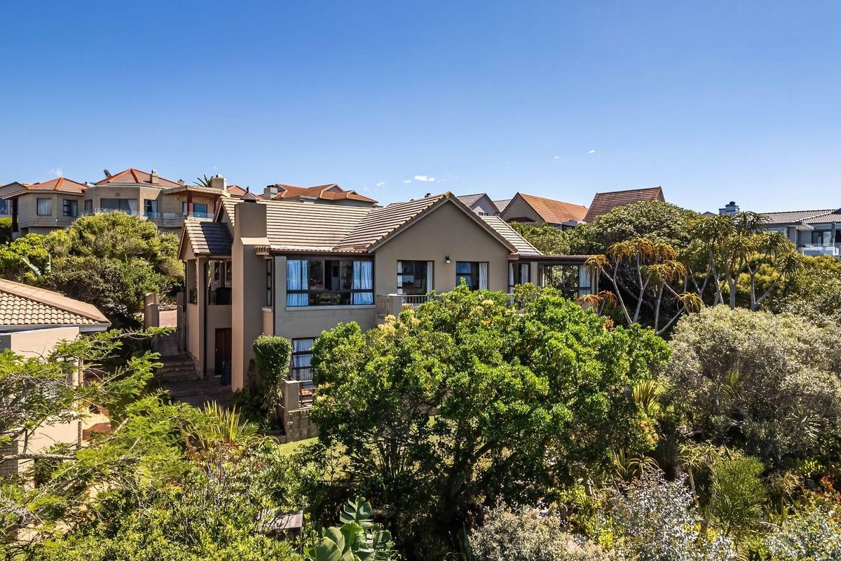 An elevated exterior view of a multi-story residential house surrounded by mature trees and lush garden landscaping in a suburban setting.