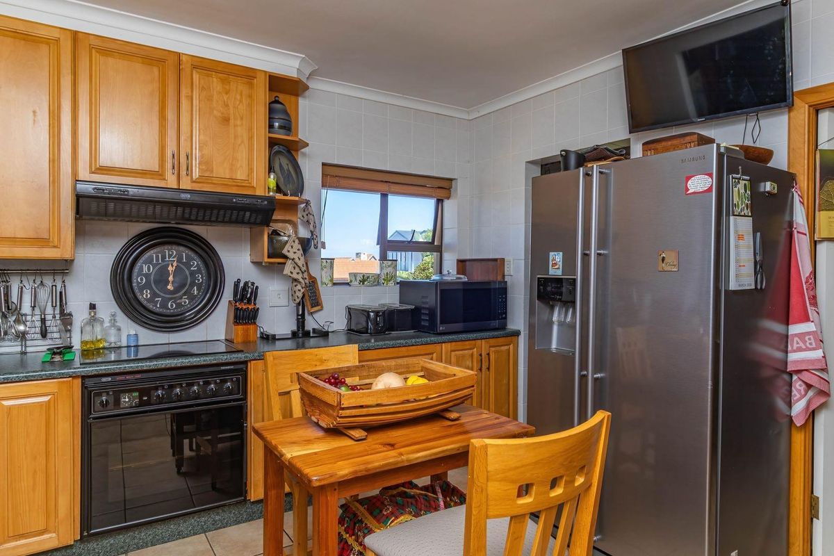 A functional kitchen featuring wooden cabinetry, tiled splashbacks, a built-in oven with extractor fan, and space for a large refrigerator.