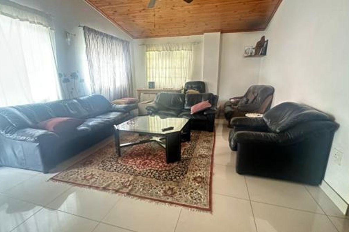 Spacious living room featuring large windows, tiled flooring, and a distinctive timber-paneled ceiling, offering a comfortable and functional family living space.