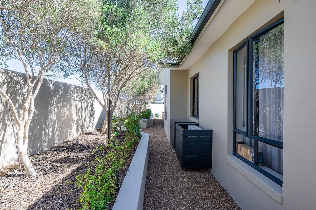 A well-maintained side garden pathway featuring a gravel walkway, retaining wall, and established trees along the property boundary.