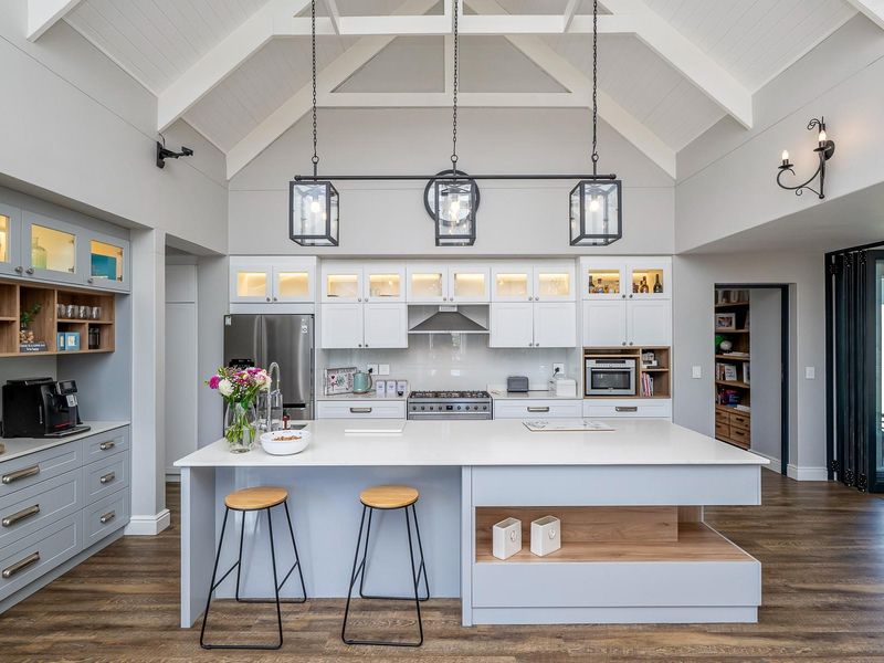 Modern kitchen featuring a large central island, quartz countertops, high-end built-in appliances, and a striking vaulted ceiling with pendant lighting.