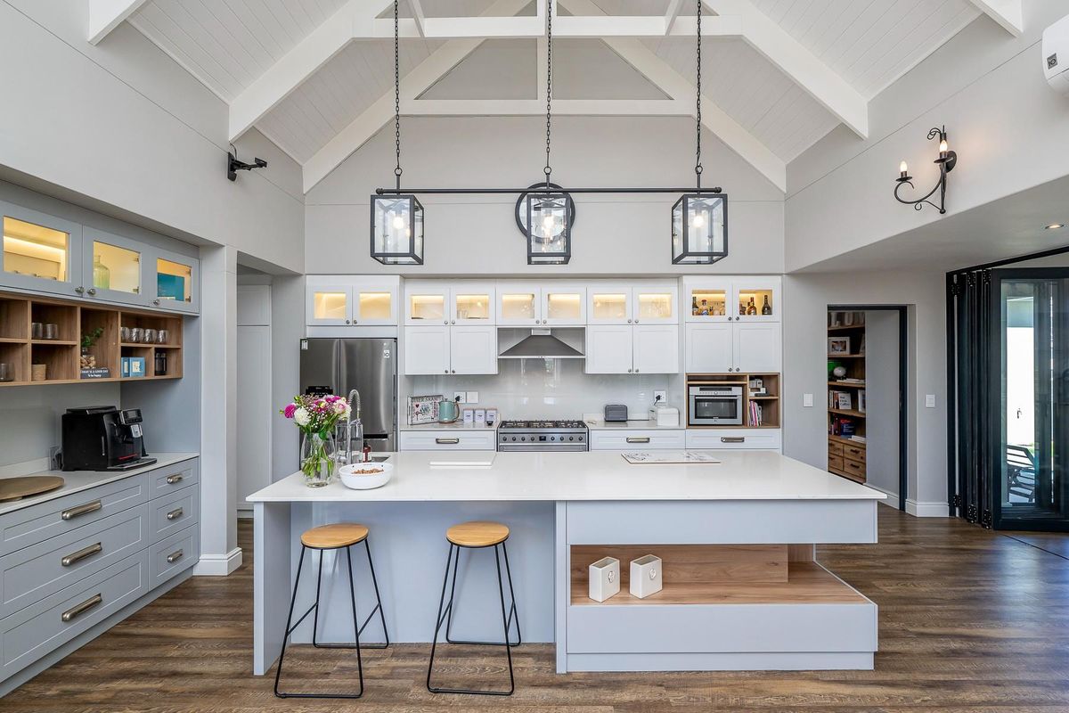 Modern kitchen featuring a large central island, quartz countertops, high-end built-in appliances, and a striking vaulted ceiling with pendant lighting.