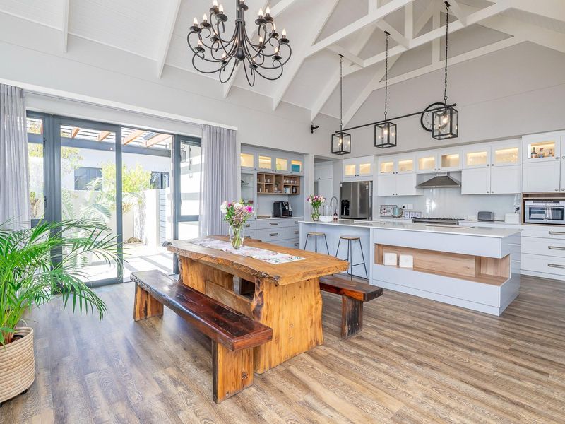 Spacious open-plan kitchen and dining area featuring a vaulted ceiling with exposed trusses, modern cabinetry, a central island, and seamless access to the patio.