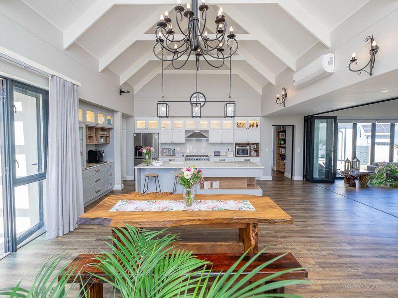 Spacious open-plan living and kitchen area featuring a vaulted ceiling with exposed rafters, modern cabinetry, a central island, and seamless access to the patio.