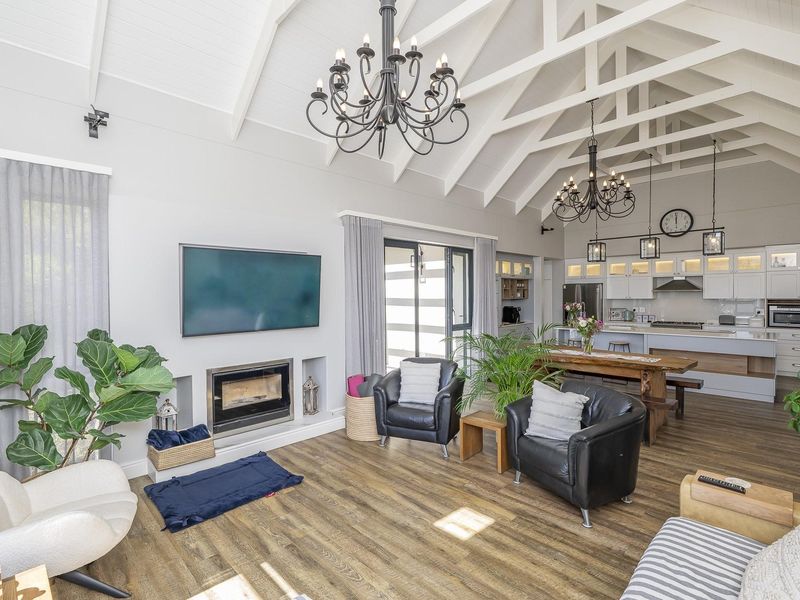 Spacious open-plan living area featuring a vaulted ceiling with exposed rafters, a modern kitchen with island, and a cozy built-in fireplace.