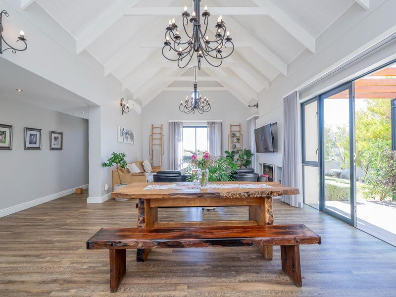 Spacious open-plan living and dining area featuring high vaulted ceilings with exposed beams, laminate flooring, and large sliding doors opening to the patio.