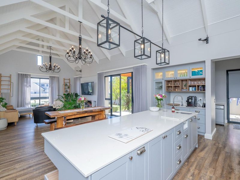 Spacious open-plan living area featuring a modern kitchen with a large island, quartz countertops, vaulted ceilings with exposed trusses, and seamless indoor-outdoor flow.