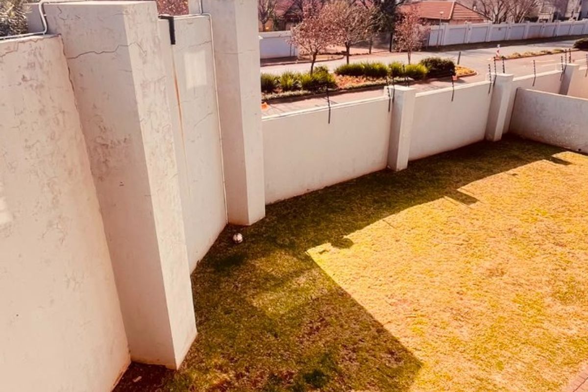 A private rear garden area featuring a paved patio section, lawn, and high perimeter boundary walls with security fencing.