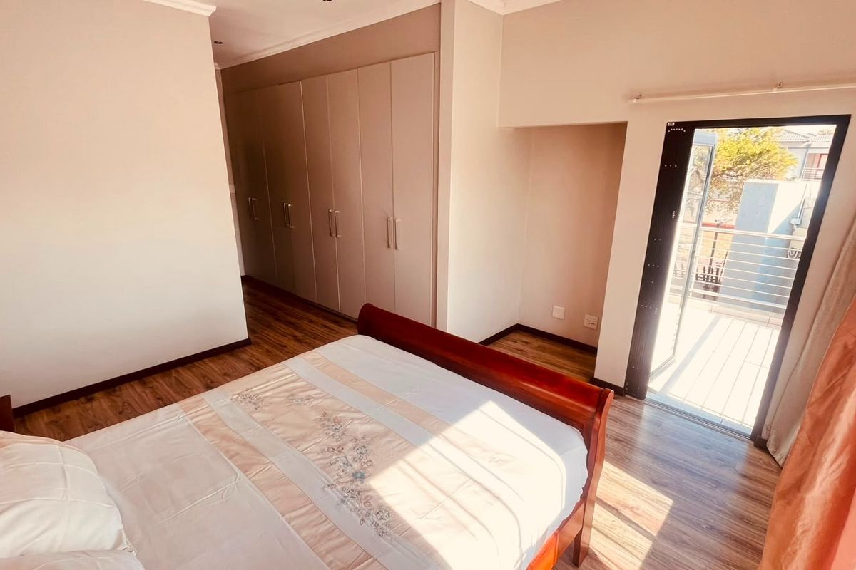 A well-maintained bedroom featuring built-in cupboards, laminate flooring, and direct access to a private balcony through a glass door.
