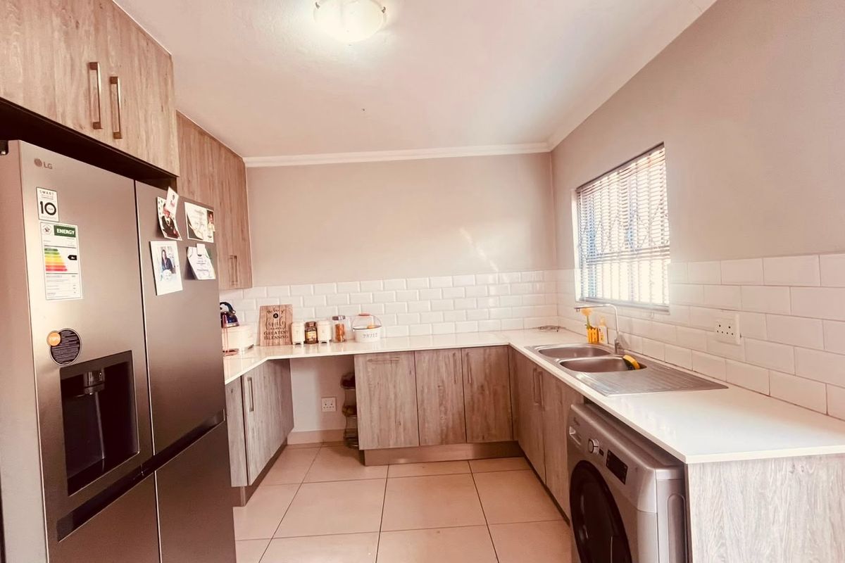 Modern kitchen featuring light wood-grain cabinetry, white subway tile backsplash, stone-look countertops, double sink, and integrated space for a washing machine.
