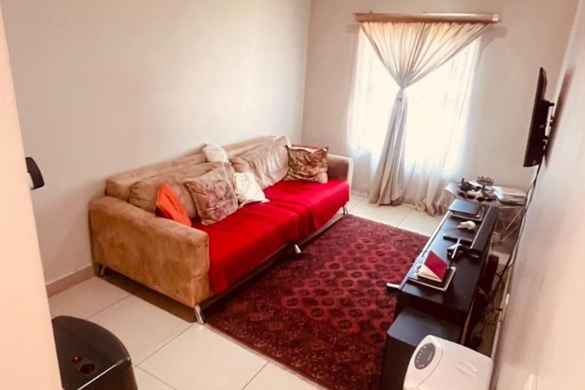 A compact living room featuring neutral tiled flooring and a window with fitted curtain rails.