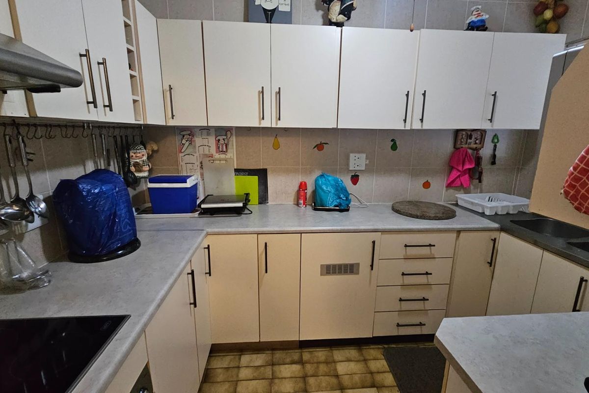 A functional kitchen featuring laminate countertops, built-in cabinetry, a stainless steel extractor fan, and a double basin sink.