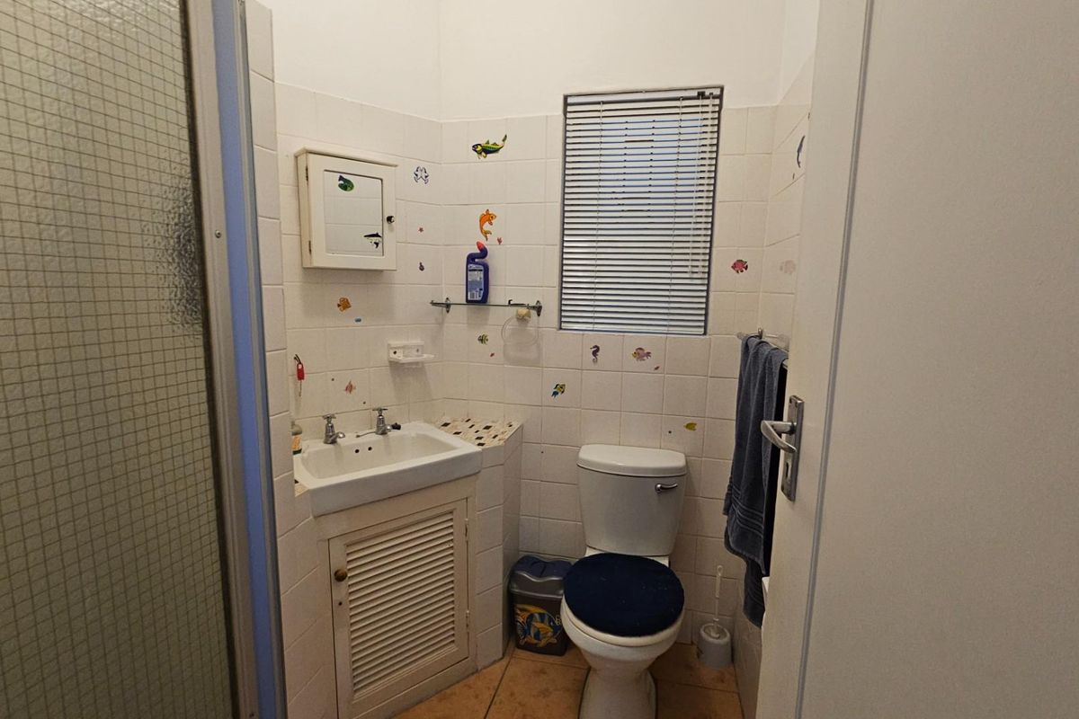 Compact bathroom featuring a pedestal-style vanity with storage, a standard toilet, and a shower enclosure with tiled walls.
