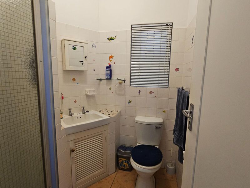 Compact bathroom featuring a pedestal-style vanity with storage, a standard toilet, and a shower enclosure with tiled walls.