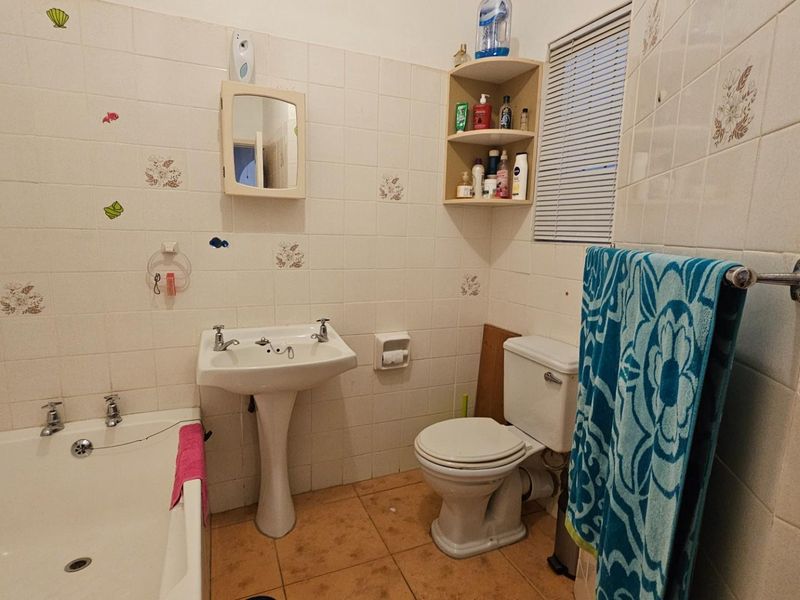 A dated bathroom featuring a pedestal sink, standard bathtub, and toilet with ceramic wall tiling and tiled flooring.