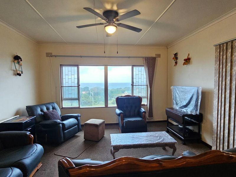 A spacious living room featuring a ceiling fan, large windows with scenic views, and carpeted flooring.