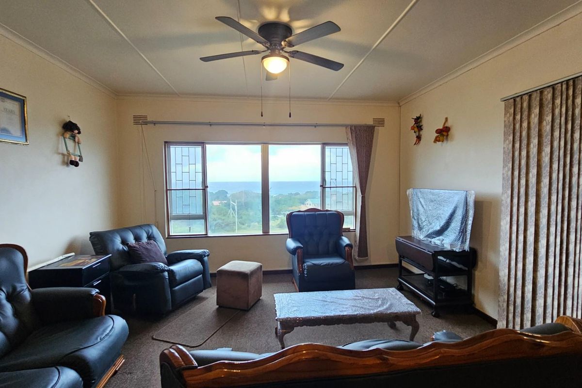 A spacious living room featuring a ceiling fan, large windows with scenic views, and carpeted flooring.