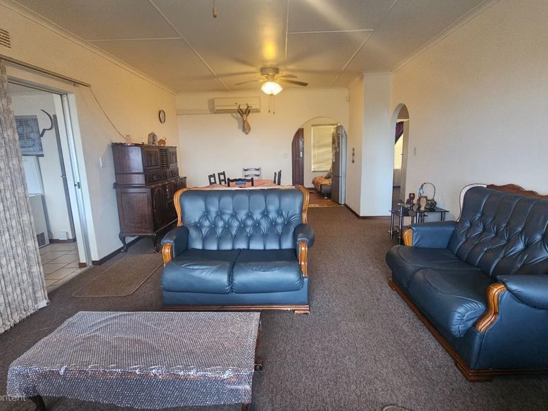 Spacious open-plan living area featuring carpeted flooring, a ceiling fan, and wall-mounted air conditioning unit, providing a functional layout for relaxation and dining.