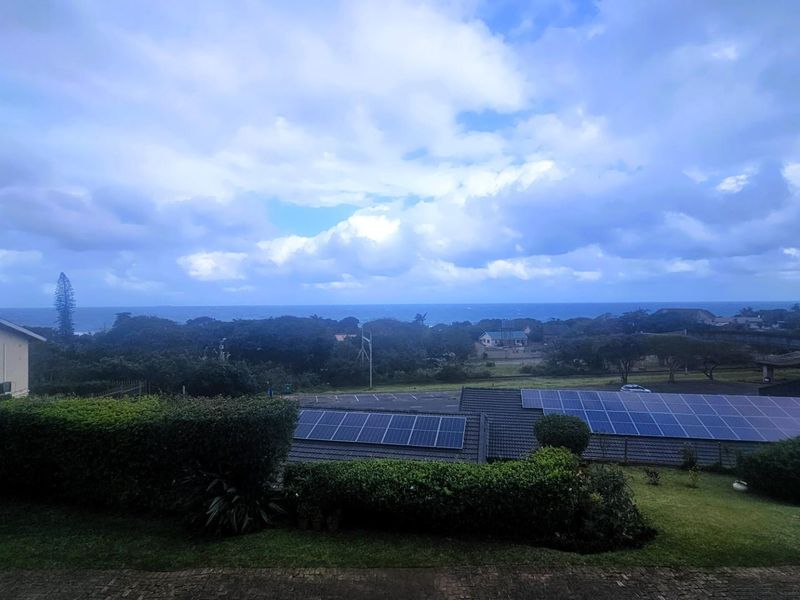 Elevated view overlooking the surrounding landscape, coastal horizon, and neighboring rooftops equipped with solar panel installations.
