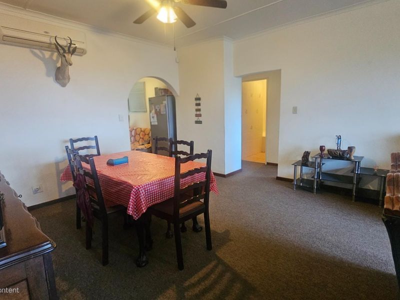 Open plan living and dining area featuring carpeted flooring, a ceiling fan, and a wall-mounted air conditioning unit.