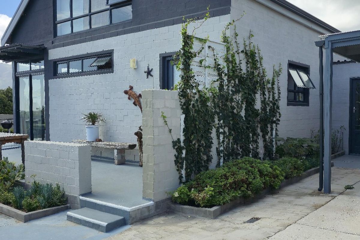 Exterior view of the property featuring a paved patio area, low brick wall, climbing plants, and a covered carport adjacent to the main structure.