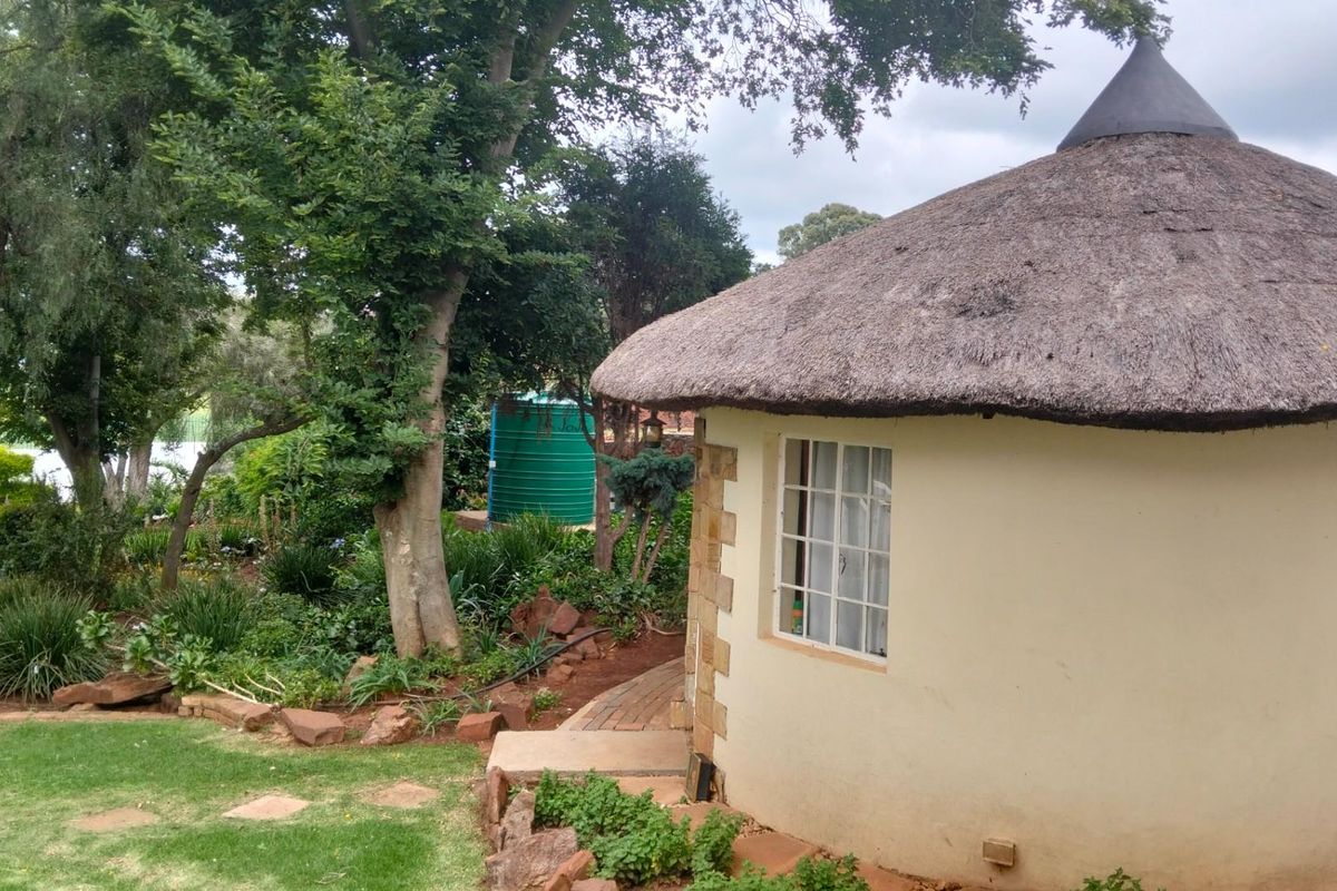 A charming rondavel-style structure with a traditional thatched roof, set within a lush, established garden on a small holding property.