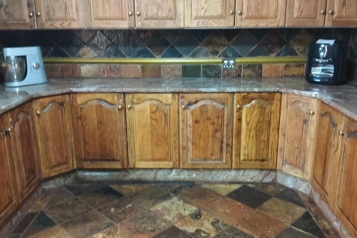 A kitchen featuring traditional wooden cabinetry, stone countertops, and a multi-toned slate tile backsplash and flooring.