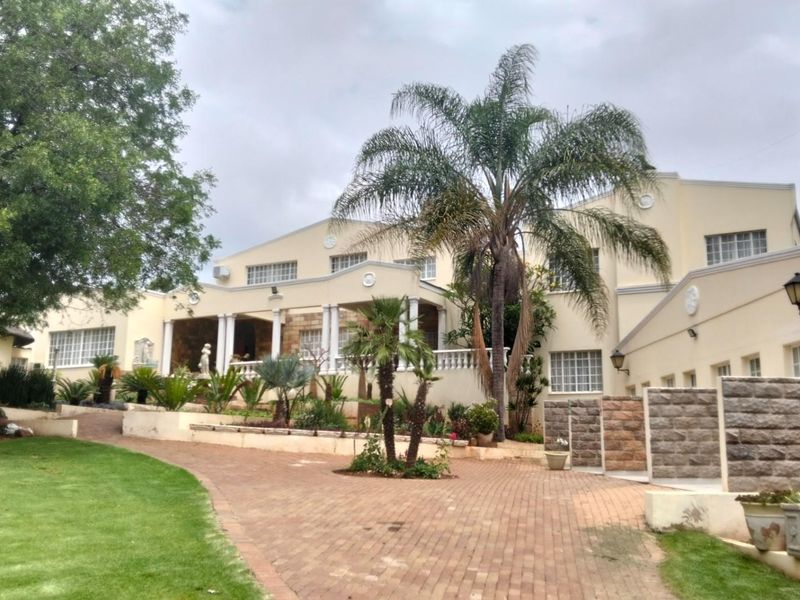 Spacious front elevation of a large residence featuring a paved driveway, manicured lawn, covered patio with columns, and established garden landscaping.