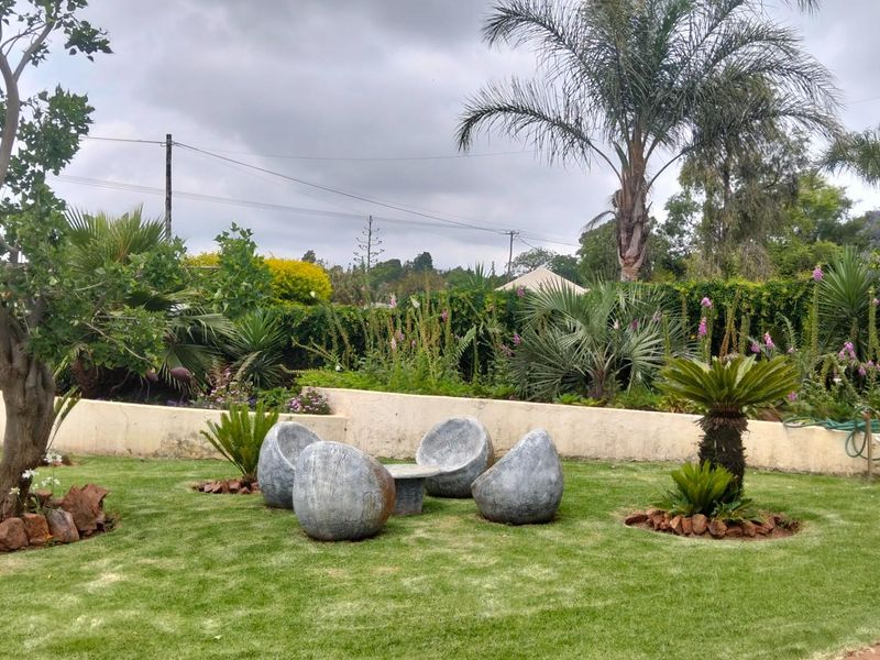A well-maintained garden area featuring a manicured lawn, mature trees, established shrubs, and a low concrete retaining wall.