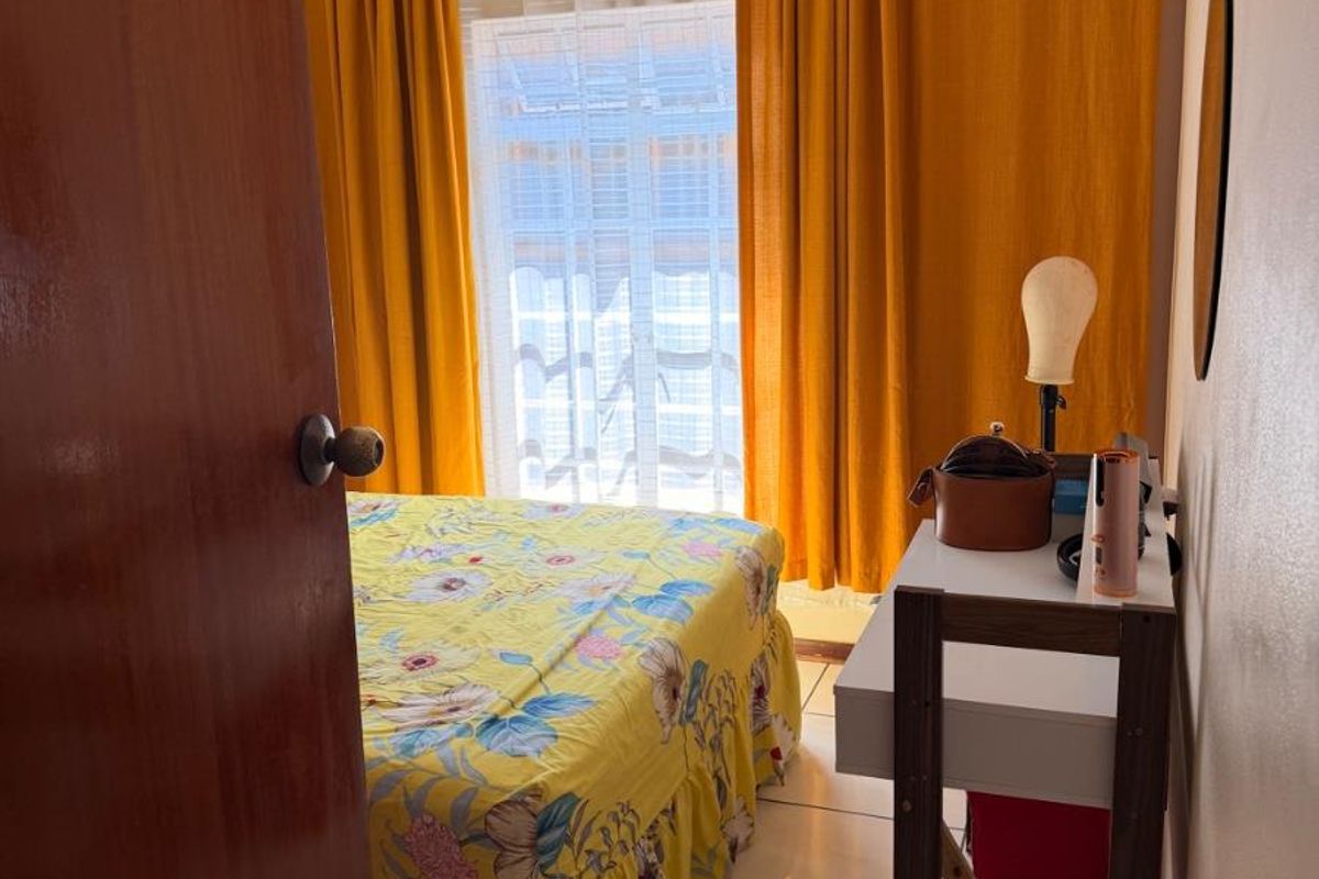 A compact bedroom featuring tiled flooring, a window with curtain tracks, and a standard wooden door.
