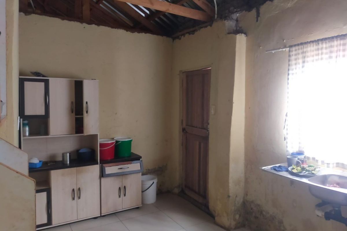A basic kitchen area featuring a sink, built-in cabinetry, and an exposed timber roof structure, requiring significant cosmetic and structural maintenance.