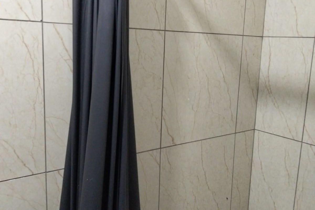 A close-up view of a bathroom shower area featuring neutral-toned ceramic wall tiles and a dark shower curtain.