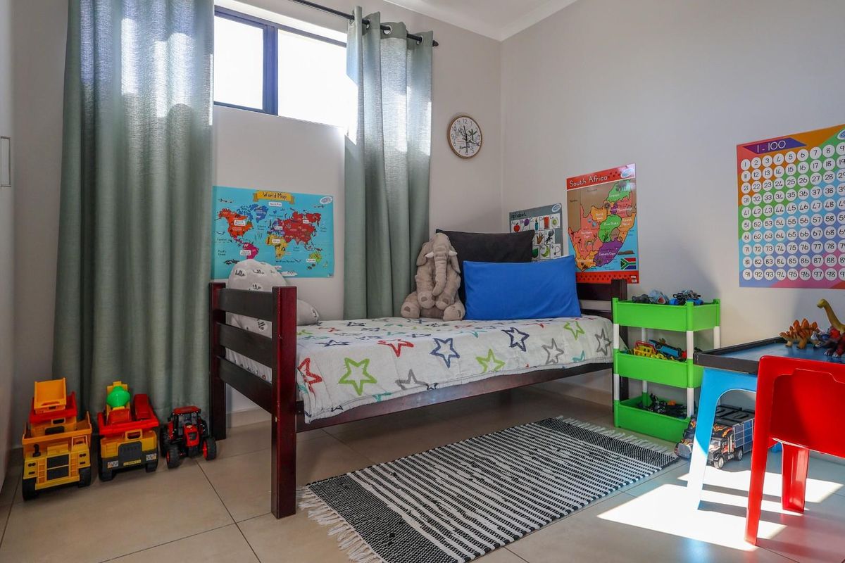 A well-maintained bedroom featuring neutral tiled flooring, built-in cupboards, and natural light through an aluminium-framed window.