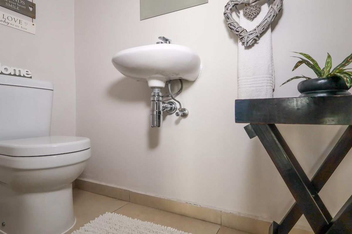 A compact guest bathroom featuring a wall-mounted basin with a chrome bottle trap and a standard toilet.