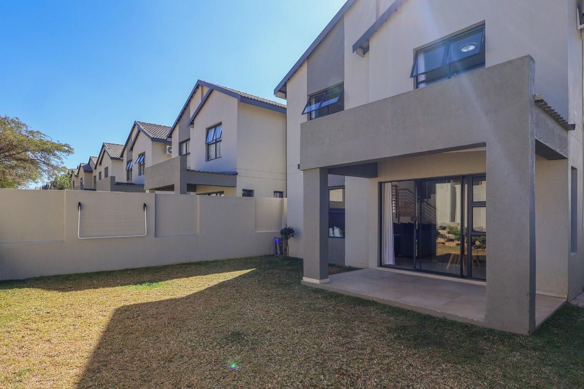 Rear view of the townhouse featuring a private garden, a covered patio area, and sliding glass doors leading into the living space.