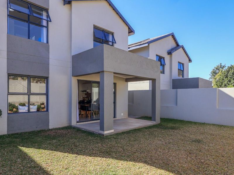 Rear view of the townhouse featuring a covered patio, sliding glass doors, and a private garden area enclosed by a perimeter wall.