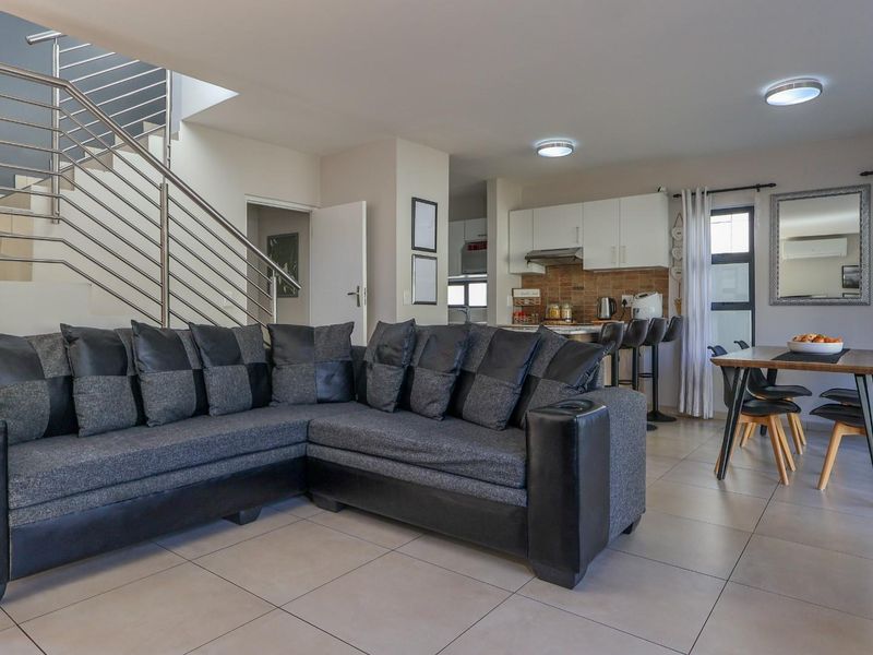 Spacious open-plan living and dining area featuring tiled floors, a modern staircase with stainless steel railing, and a functional kitchen with built-in cabinetry.
