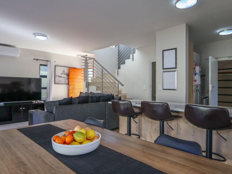 Spacious open-plan living and dining area featuring a modern kitchen island, staircase with metal balustrade, and integrated air conditioning.