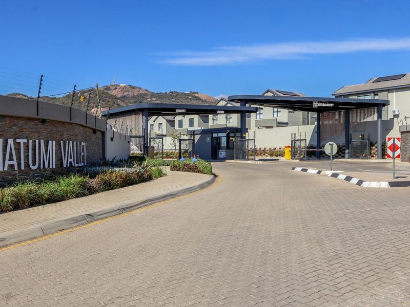 The secure entrance gatehouse of Matumi Valley townhouse complex, featuring paved access, stone-clad boundary walls, and modern security infrastructure.