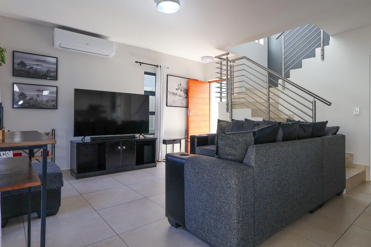 Modern living room featuring tiled flooring, a split-system air conditioner, and a staircase with a contemporary stainless steel balustrade.