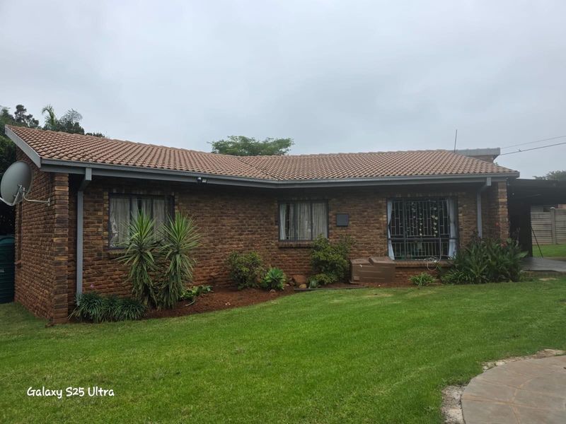 A view of the rear exterior of a brick house featuring a tiled roof, established garden, and security bars on the windows.